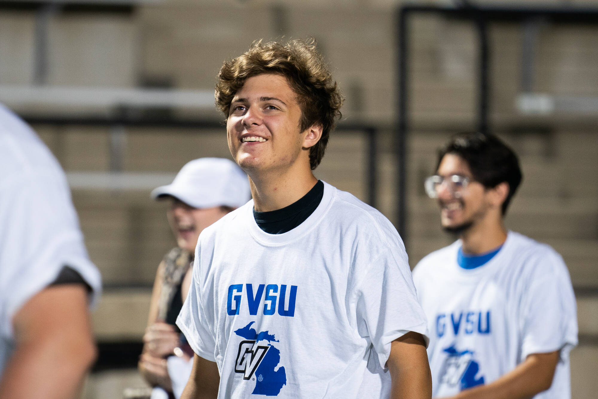 A young person in a white T-shirt with GVSU logo smiles at an outdoor event.